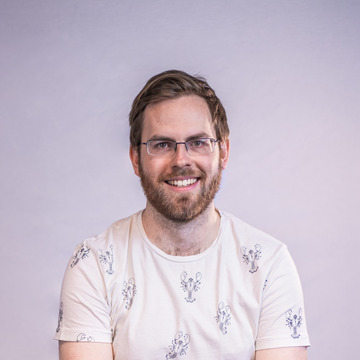 Headshot of Murray, a white-skinned person with a beard, glasses, and mid-length brown hair with a slight quiff. They are smiling and wearing a white t-shirt with miniature black lobsters printed on it.